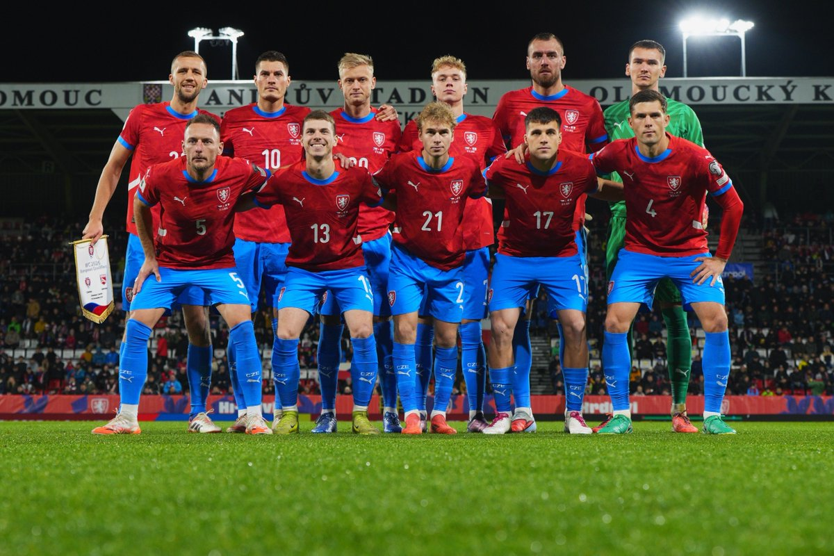 Czech Republic soccer team posing together on stadium pitch under bright lights, wearing red jerseys and blue shorts.