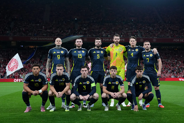 Scotland national soccer team poses on field in dark kits before kickoff, goalkeeper in neon green.