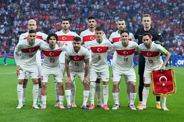Turkey national football team posing in white kits with red crescent flags before a stadium crowd.