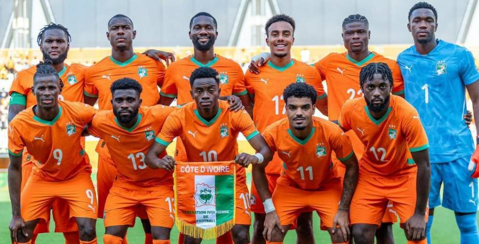 Ivory Coast national football team posing in orange uniforms, holding a Côte d’Ivoire banner on a field.