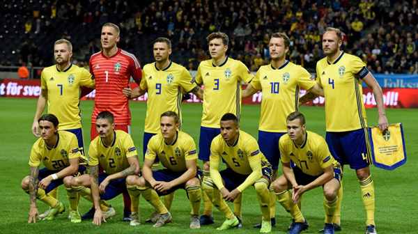 Swedish national soccer team in yellow uniforms posing on field before match, with goalkeeper holding blue kit.