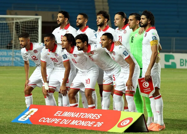 Tunisian national soccer team stands in a line on the field before a match, wearing white kits.