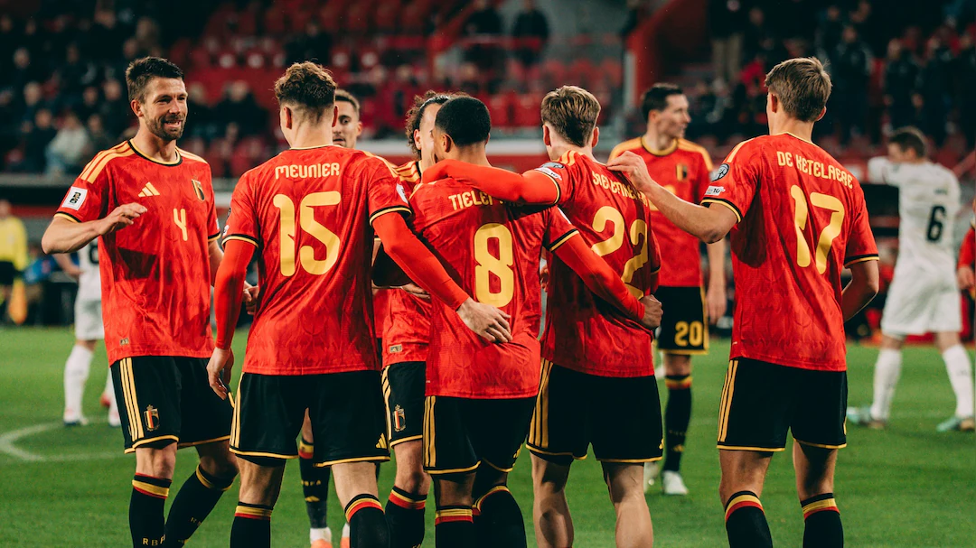 Soccer players in red jerseys celebrate together on the field, arms around each other in a stadium. Belgium.