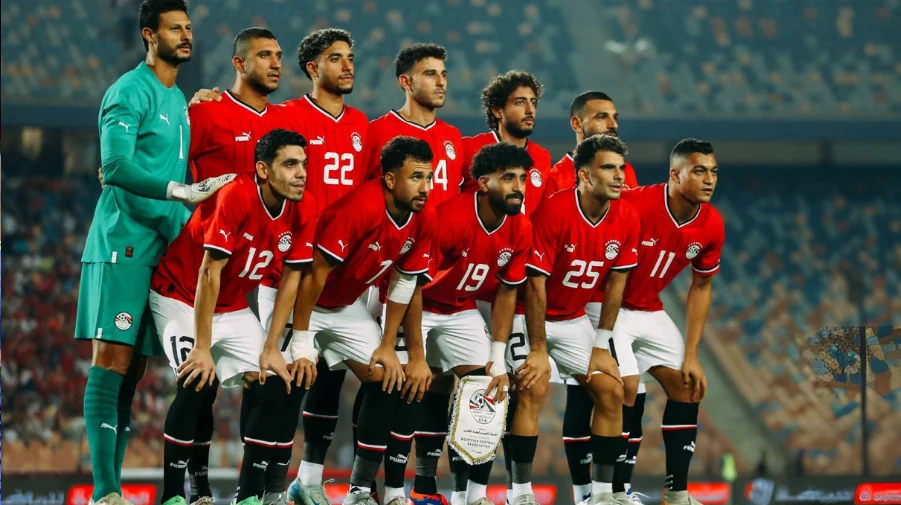 Soccer team lineup in red uniforms with goalkeeper in green, standing together on stadium field. Egypt