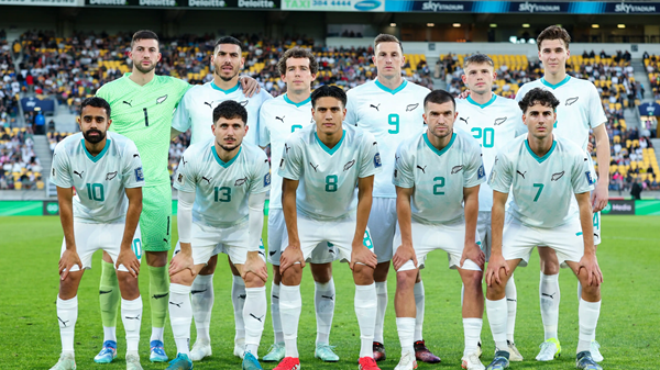 New Zealand national soccer team posing for a lineup photo on a stadium pitch, players in light green kits.