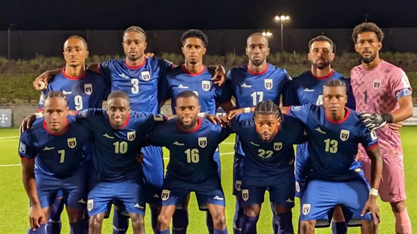 Men’s soccer team posing together on a field at night, wearing blue and pink uniforms. Cape Verde