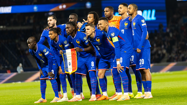 Soccer team in blue kits lines up on field, posing together before a match under stadium lights. France