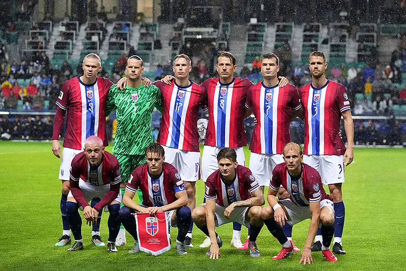 Football team lineup posing on snowy stadium pitch in red, white, and blue kits. Norway