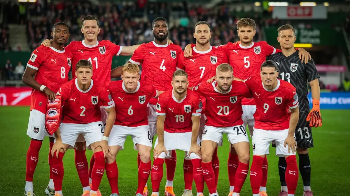 Austria national soccer team poses in red uniforms on a stadium pitch, with goalkeeper in black.