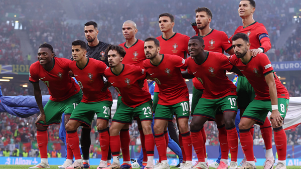 Portugal national football team players in red and green kits posing together on a stadium pitch.