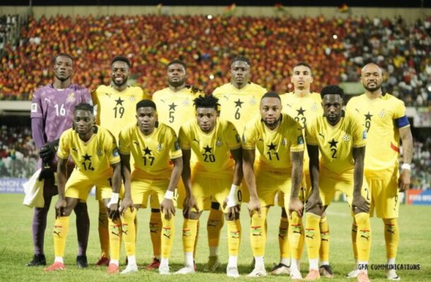 Ghana soccer team lineup in yellow uniforms posing on field before a match, stadium crowd behind.